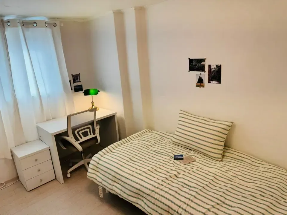 A small one-room studio with a bed, desk and window