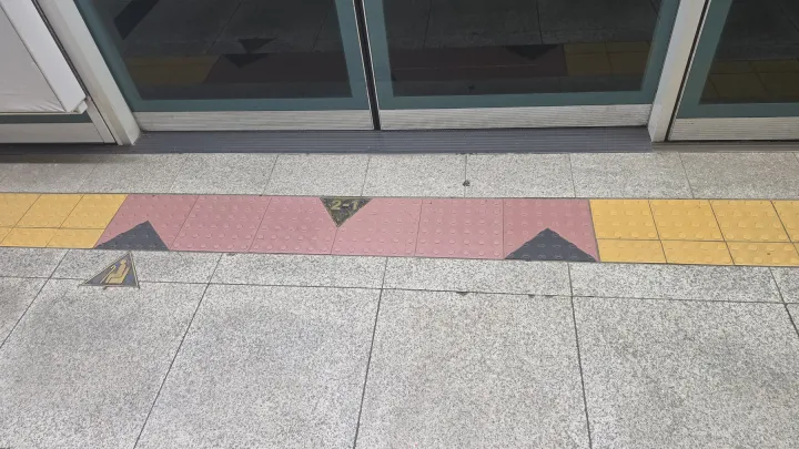 A Seoul subway platform floor marked 2-1 in front of the screen doors, showing the car and door number
